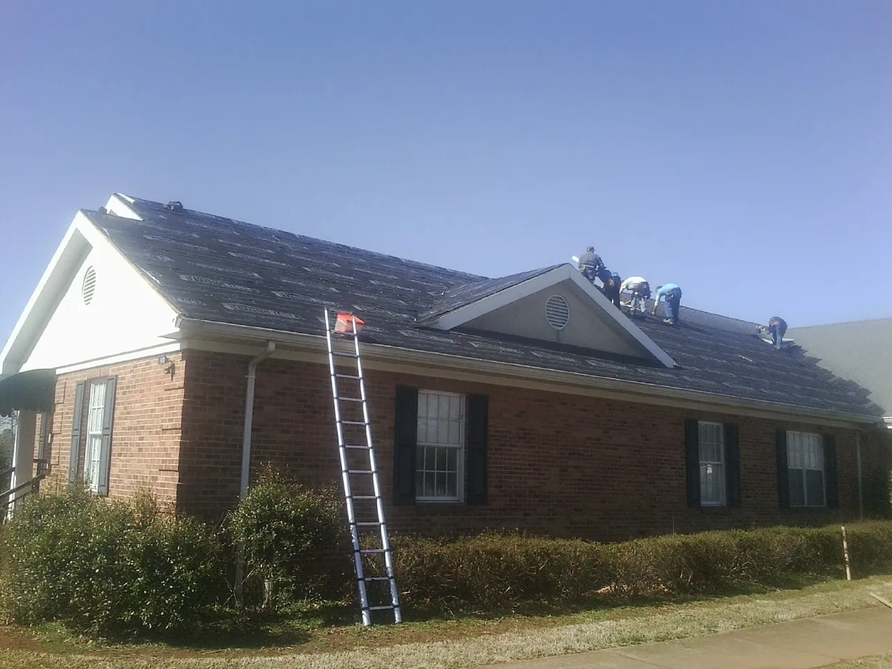 Crew tearing shingles off a brick ranch roof with a ladder set — Emergency Roof Repair work by our crew in Stillman Valley