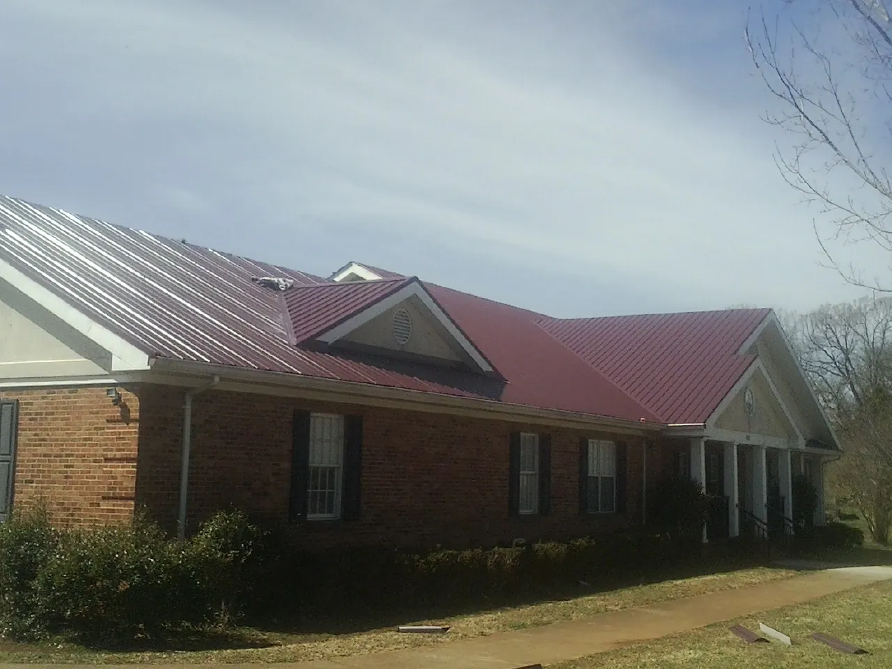 Red metal roof with gabled entries on a long brick building, from a Hail Damage Roof Repair job in Stillman Valley