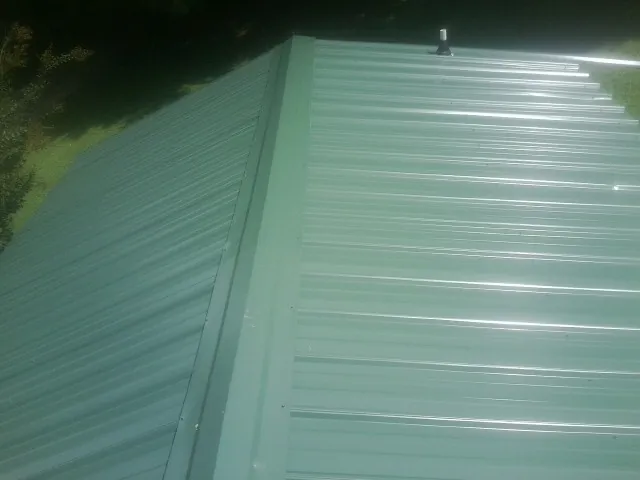 New green metal panels meeting at the ridge of a roof — Flat Roof Repair work by our crew in Stillman Valley
