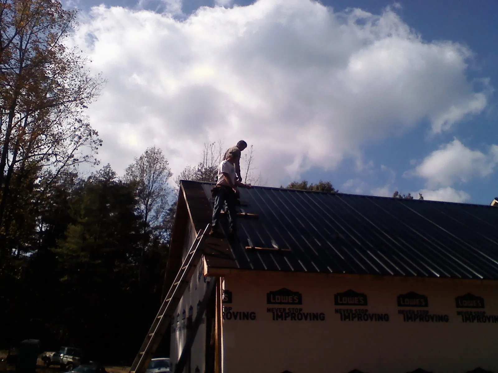 Roofer fastening dark metal panels high against a cloudy sky in Stillman Valley