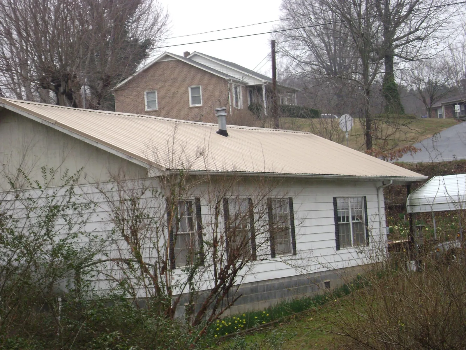 Tan metal roof on a white sided house set into a hillside — Commercial Roofing by Roofing Brothers in Stillman Valley