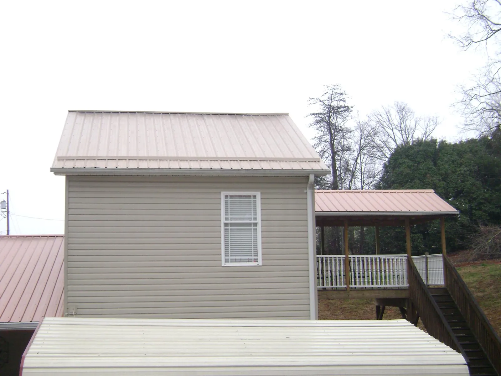 Tan metal roofs on a two story addition and attached porch, from a Roof Replacement job in Stillman Valley